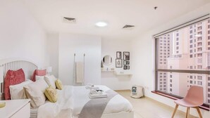 A modern bedroom with a large window, a bed with white bedding, a pink chair, and a small bedside table. - StayShort - Modern 2BR Retreat with Breathtaking Views in JBR (Dubai)