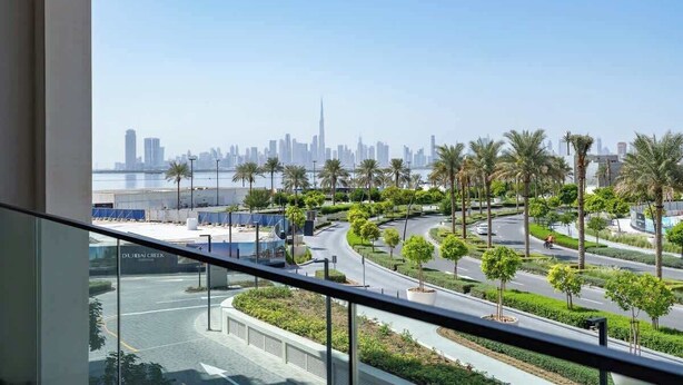 A view from a balcony overlooking a landscaped area with palm trees and a curved road, with a city skyline in the background.