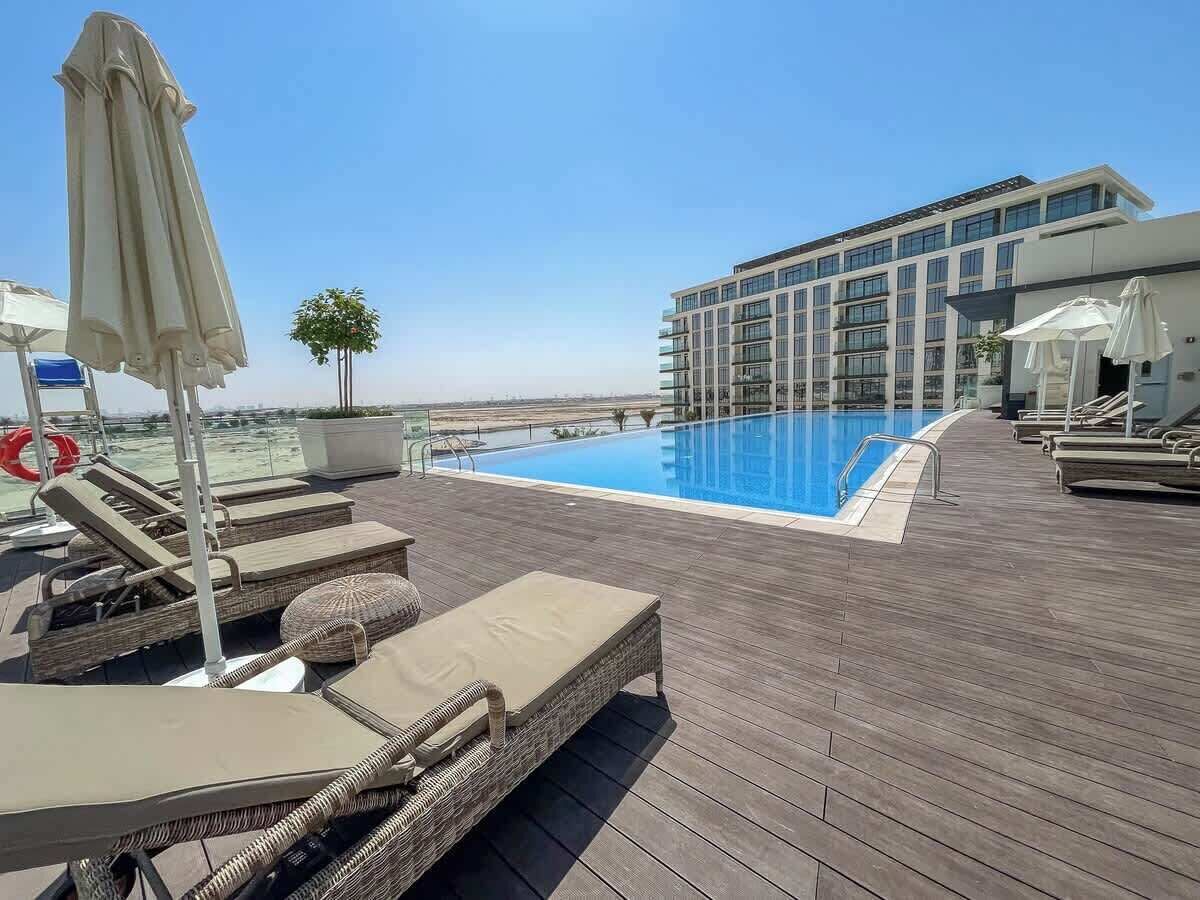 A rooftop pool area with lounge chairs and umbrellas, a clear blue pool, and a modern building in the background.