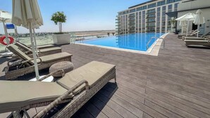A rooftop pool area with lounge chairs and umbrellas, a clear blue pool, and a modern building in the background.