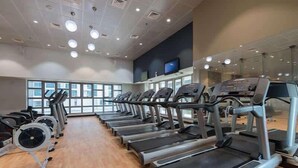 Une salle de sport avec des tapis de course disposés en rangées, de grandes fenêtres et un plafond plat doté d’un éclairage encastré.