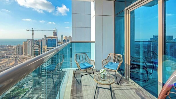 Ein Balkon mit Glastrennwand, zwei Korbstühle mit Kissen und Blick auf Stadt und Autobahn.