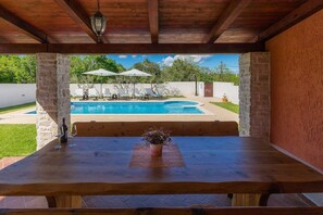 Une table en bois ornée d’un vase de fleurs, d’une bouteille et de verres, donnant sur une piscine bordée de chaises longues et de parasols.