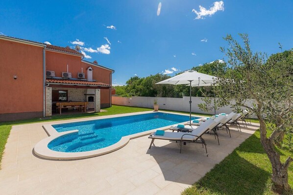 Une piscine avec des chaises longues et un espace barbecue.