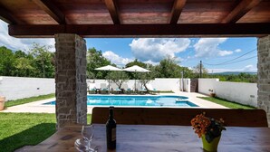 A wooden table with a bottle and a glass, overlooking a swimming pool with lounge chairs and umbrellas. - Villa Prisedi in Rakalj (Rakalj)