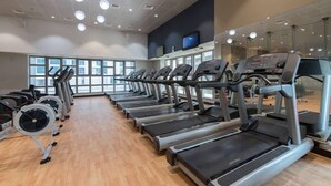 A gym with multiple treadmills lined up, large windows, and a television on the wall. - StayShort - Scenic 2BR Apartment in Dubai Marina Near the Beach (Marina/JBR)