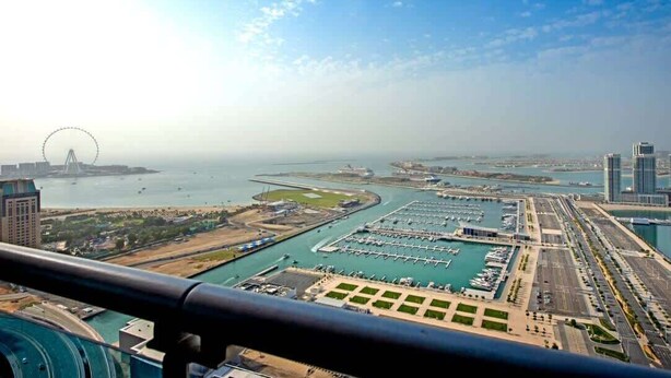 An aerial view of a marina with boats docked, a large Ferris wheel in the background, and a modern cityscape with high-rise buildings. - StayShort - Scenic 2BR Apartment in Dubai Marina Near the Beach (Marina/JBR)