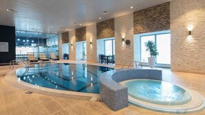 An indoor swimming pool with a hot tub, surrounded by stone walls and large windows. - StayShort - Scenic 2BR Apartment in Dubai Marina Near the Beach (Marina/JBR)
