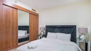 A hotel room with a large bed, a wardrobe with a mirror, bedside lamps, and a vanity with drawers. - StayShort - Scenic 2BR Apartment in Dubai Marina Near the Beach (Marina/JBR)