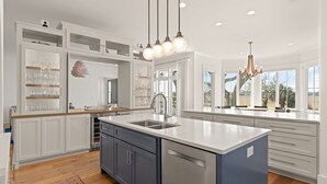 A modern kitchen with white cabinetry, a large island, and pendant lighting. - Sunset Peak sleeps 12 with a pool (St Simons Island)