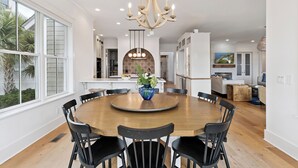 A spacious dining area with a round wooden table surrounded by black chairs, a chandelier, and a decorative vase. - Sunset Peak sleeps 12 with a pool (St Simons Island)