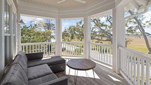 A covered porch with a wooden ceiling, white railings, and a gray sofa. - Sunset Peak sleeps 12 with a pool (St Simons Island)