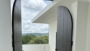 A view through a dark wooden door into a balcony with a tiled floor and a white wall. - Hotel Mysore Radiance (Mysore)