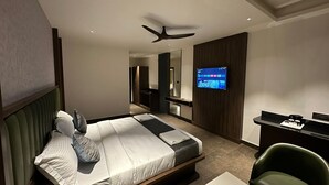 A modern hotel room with a bed, a desk, a television, and a ceiling fan. - Hotel Mysore Radiance (Mysore)