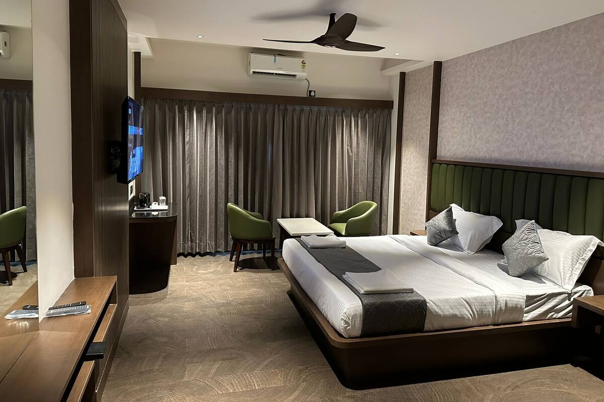 A modern hotel room with a bed, a desk, a chair, a television, and a ceiling fan.