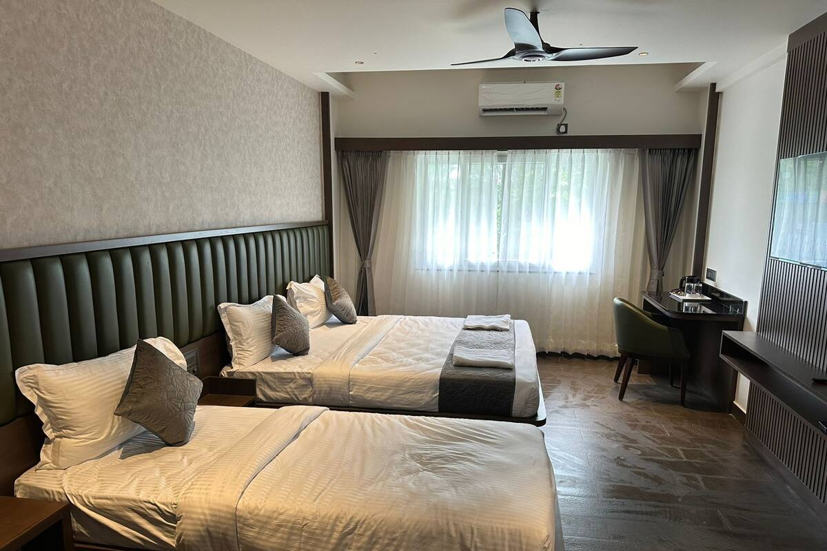 A hotel room with two beds, a desk, a chair, an air conditioning unit, and a ceiling fan.
