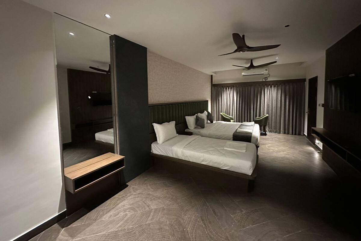 A modern hotel room with a large bed, a seating area with chairs, a television, and a ceiling fan.