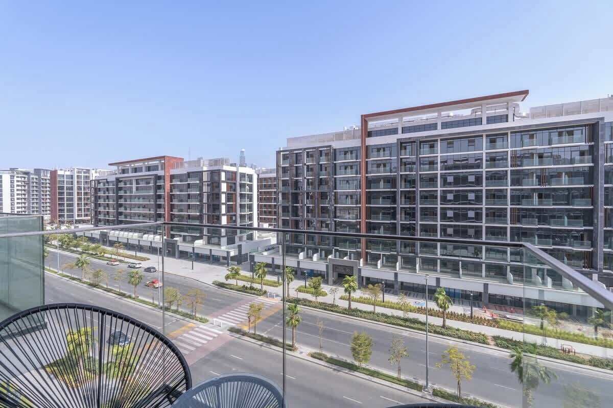 Ein modernes Mehrstöckgebäude mit großen Fenstern, umgeben von einer gepflegten Grünanlage mit Bäumen und einer Straße.
