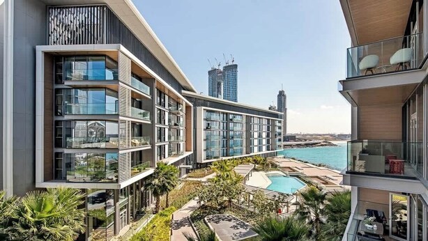A modern hotel with multiple balconies, a pool area, and views of the city skyline and ocean. - StayShort - Delightful 1BR in Bluewaters Island - JBR Walk! (Bluewaters Island)