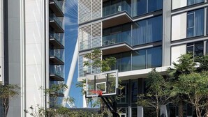 An outdoor basketball court with a basketball hoop, surrounded by trees and modern buildings. - StayShort - Delightful 1BR in Bluewaters Island - JBR Walk! (Bluewaters Island)