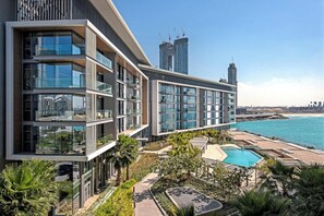 A modern multi-story building with balconies, a swimming pool, and a view of the sea and city skyline.