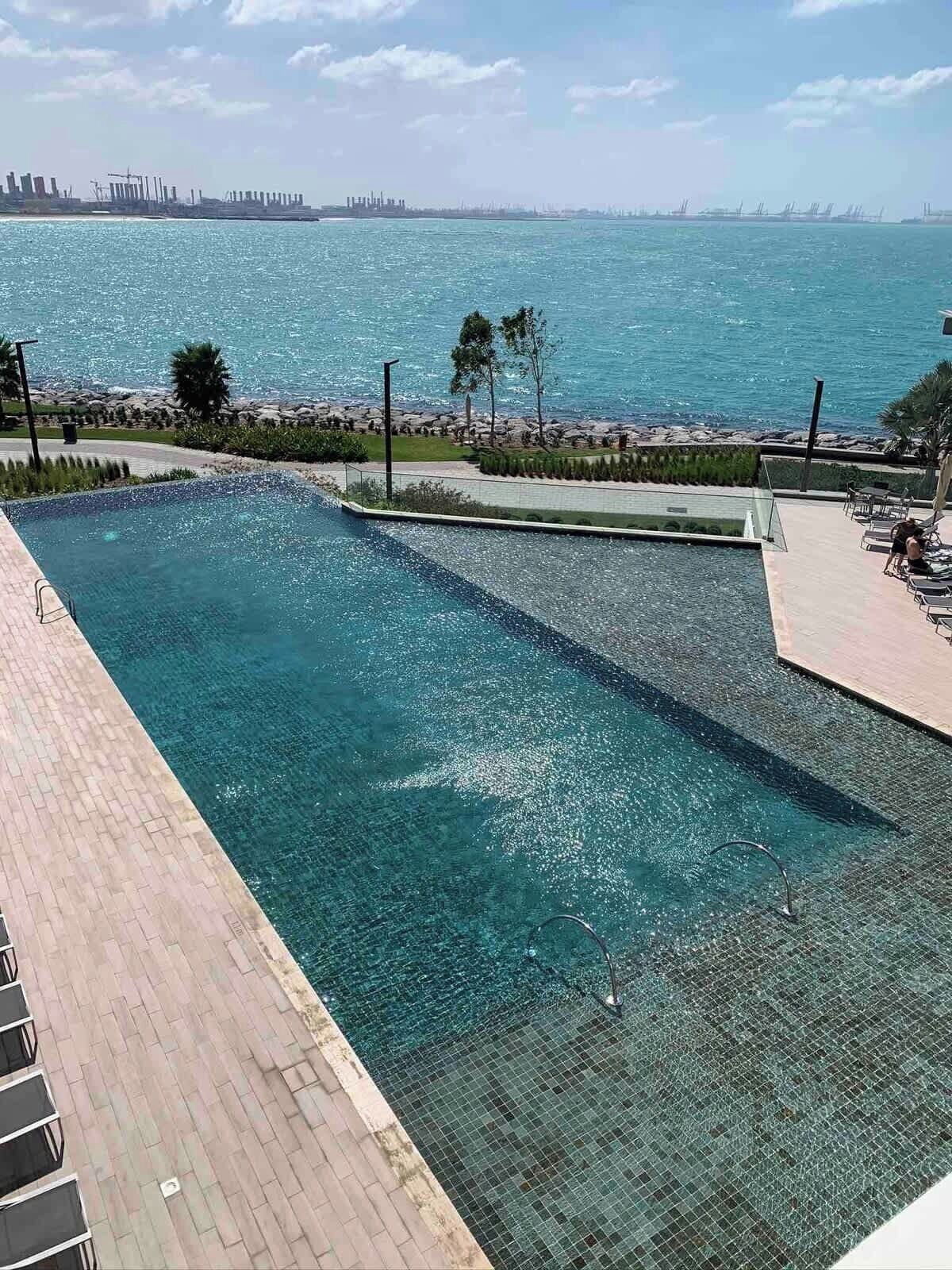 A swimming pool with a view of the sea and a distant city skyline.