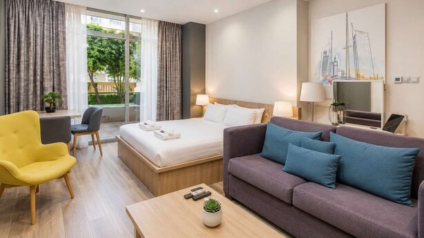 Una habitación de hotel con cama, sofá, sillón, mesa de centro y televisor.