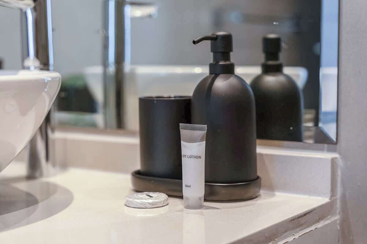 Un baño con un lavamanos blanco, un dispensador de jabón negro y una loción corporal en la encimera.