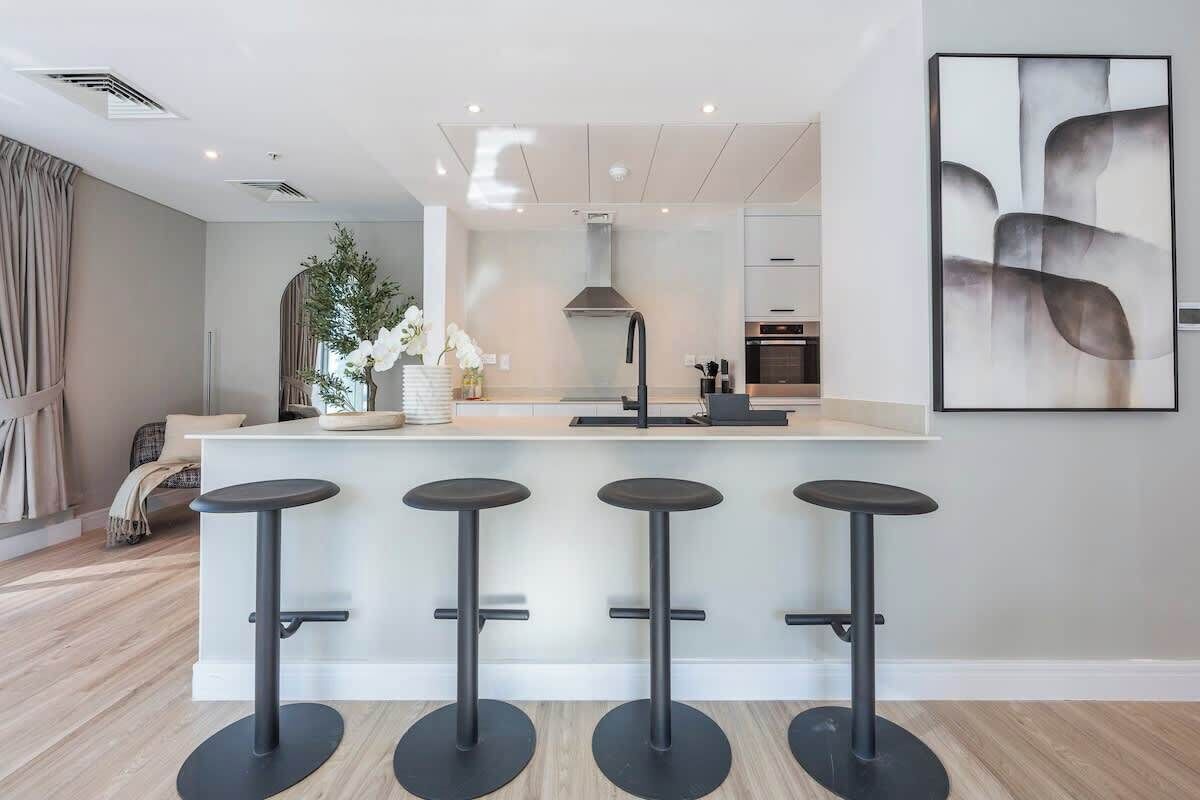 A modern kitchen with a central island, bar stools, and a large window.