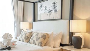 A hotel room with a bed, two bedside lamps, a framed picture of palm trees, and a nightstand with a lamp. - StayShort - Elegant & Spacious 4BR for Families in Creek Harbour (Dubai)