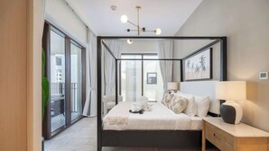 A modern bedroom with a four-poster bed, a bedside table with a lamp, and a large window with curtains. - StayShort - Elegant & Spacious 4BR for Families in Creek Harbour (Dubai)