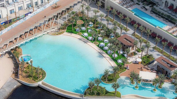 An aerial view of a resort with a large central pool, multiple smaller pools, and outdoor seating areas surrounded by palm trees. - StayShort - Elegant & Spacious 4BR for Families in Creek Harbour (Dubai)