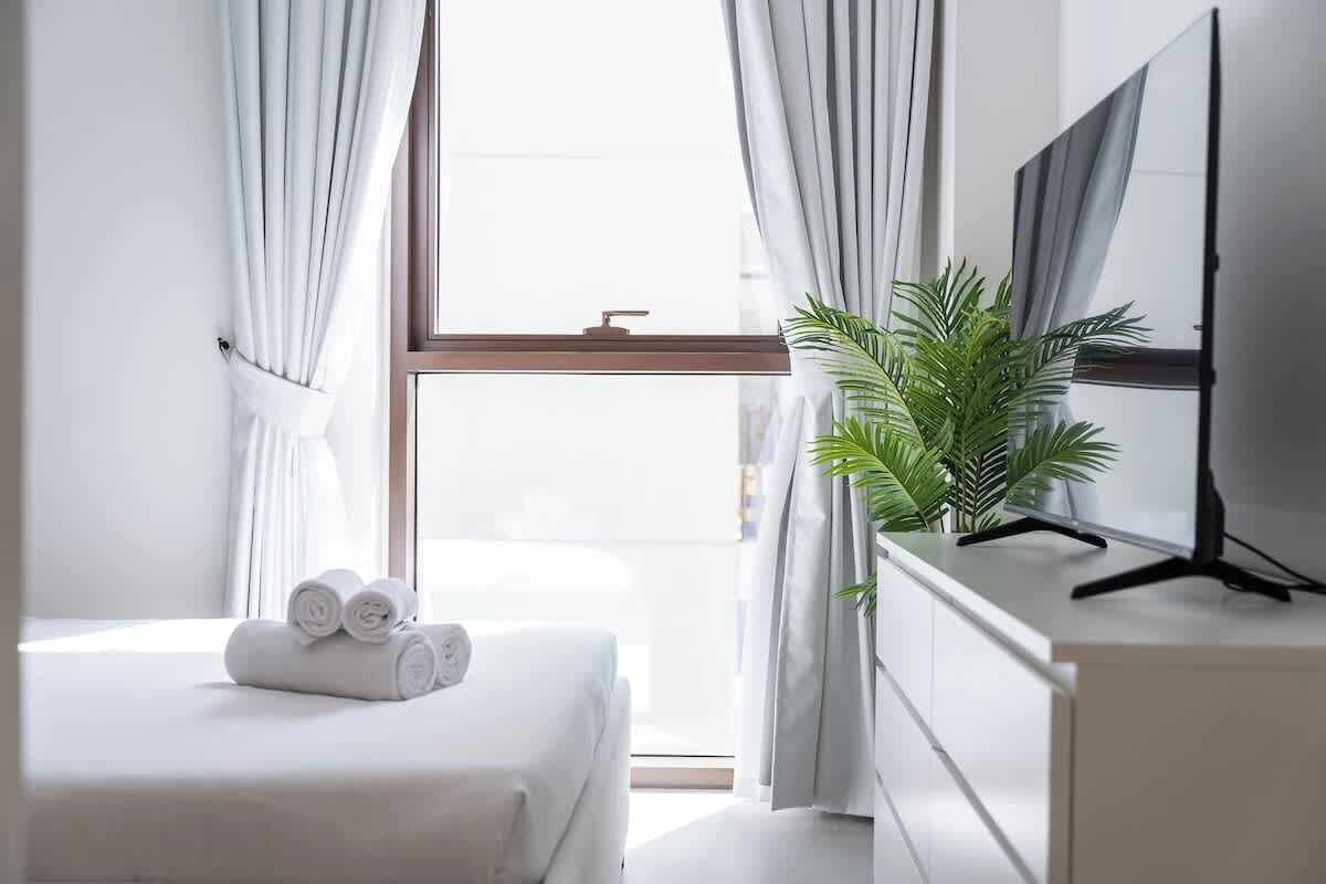 Ein Hotelzimmer mit Bett, Fernseher auf einem Schrank, einem Fenster mit Vorhängen und einer Zimmerpflanze.