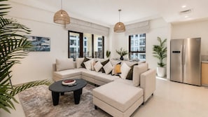 A modern living room with a sectional sofa, a round coffee table, and a built-in stainless steel refrigerator.