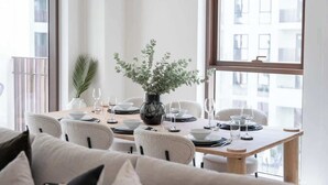 A dining area with a table set for four, a vase with greenery, and a city view through large windows. - StayShort - Elegant & Spacious 4BR for Families in Creek Harbour (Dubai)