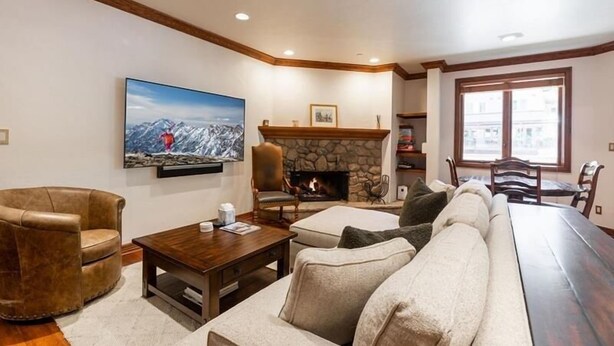 A cozy living room with a stone fireplace, a large flat-screen TV, leather armchairs, and a wooden coffee table. - Strawberry Park 109 2 Bedroom Condo (Avon)