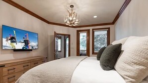 A bedroom with a large bed, a television mounted on the wall, and a chandelier. - Strawberry Park 109 2 Bedroom Condo (Avon)