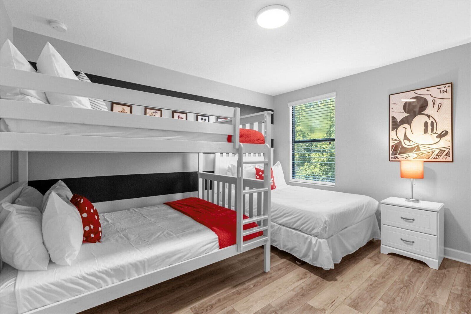A bunk bed room with a window, a nightstand, and a Mickey Mouse themed wall art.
