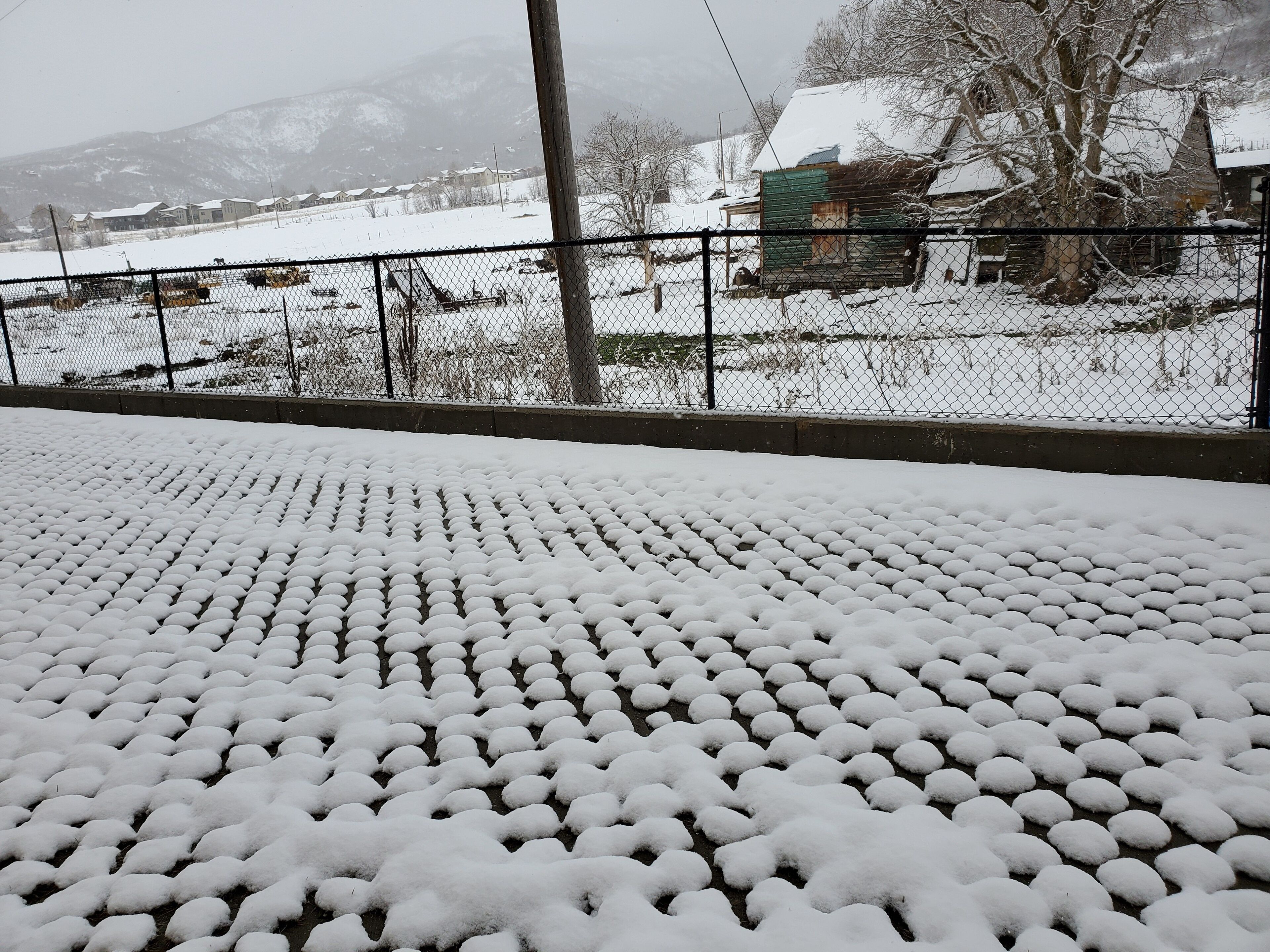 Zona exterior cubierta de nieve, con una valla metálica y vistas a un paisaje rural al fondo.