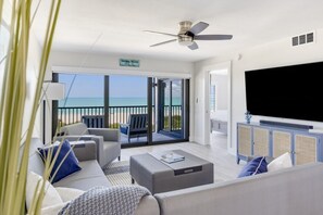 A modern living room with a large TV, comfortable seating, and a view of the ocean. - Pelicans Roost 307 2 Bedroom Condo (Sanibel)