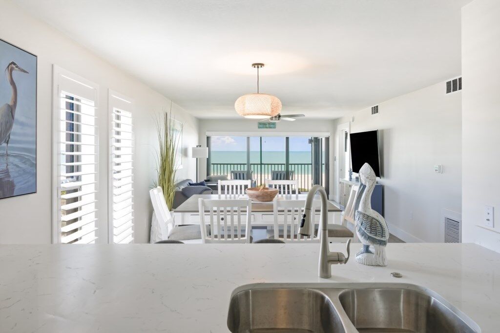 Una cocina moderna con una isla grande, un comedor con mobiliario blanco y vistas al océano a través de amplios ventanales.