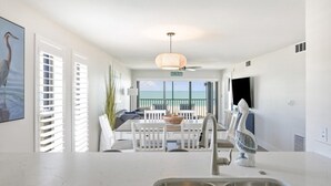 Une cuisine moderne dotée d’un grand îlot central, d’un coin repas avec des meubles blancs et offrant une vue sur l’océan grâce à de grandes fenêtres.