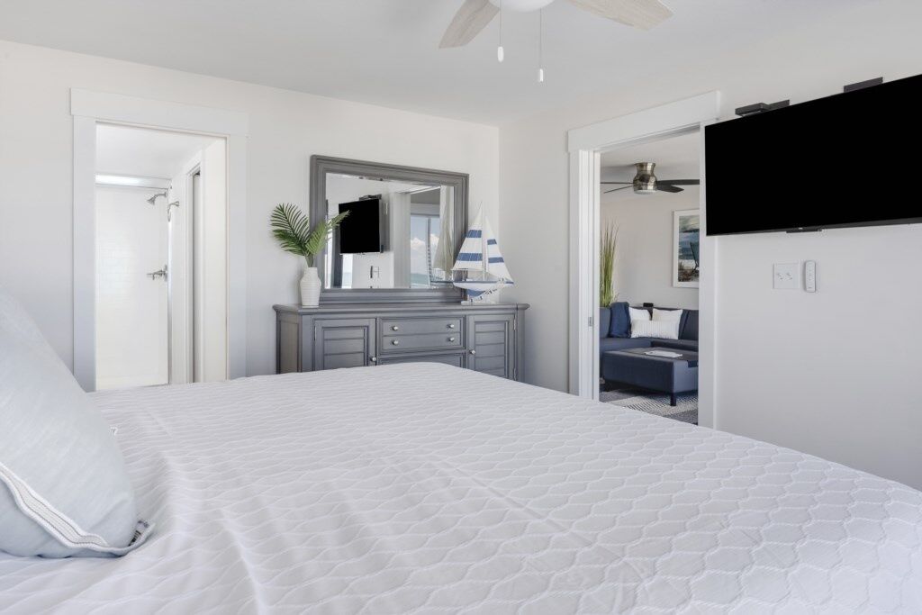 A bedroom with a large bed, a dresser, a mirror, and a TV.