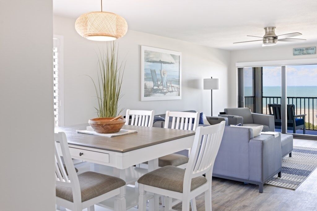 A modern living room with a dining area, white furniture, a large window with a view, and a ceiling fan.