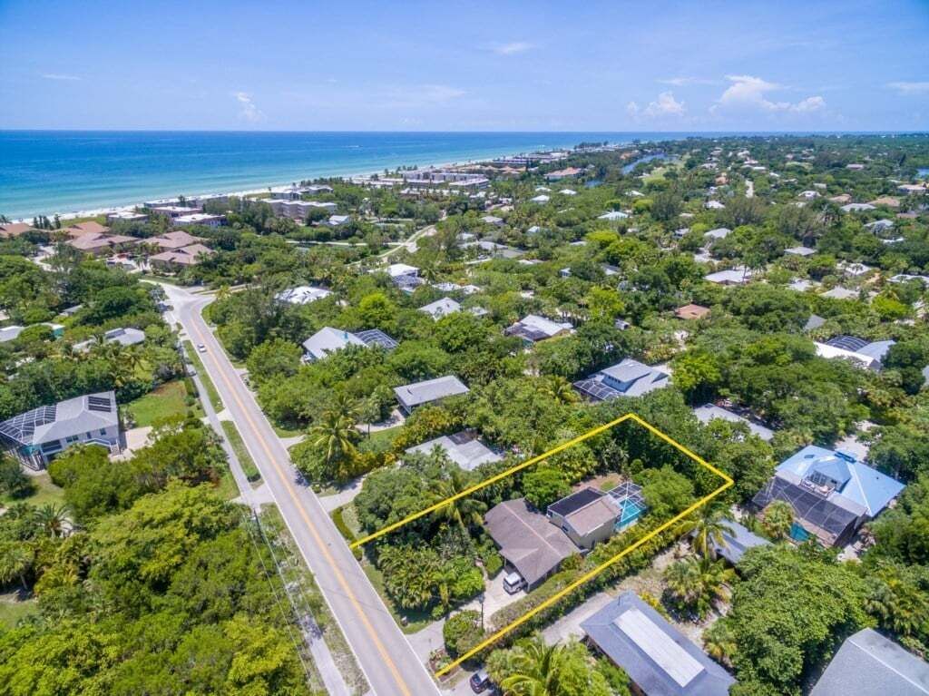 An aerial view of a residential area with houses, a road, and a beach in the background.
