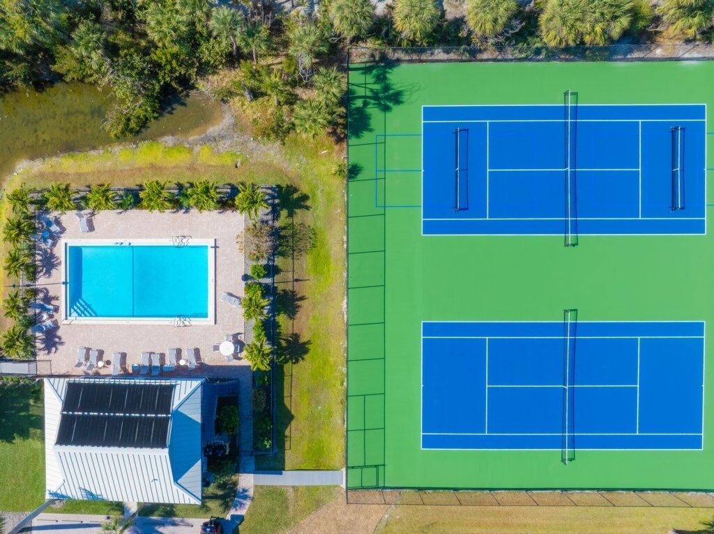 An aerial view of a property with a swimming pool, tennis courts, and a building with a sloped roof.