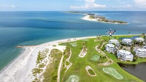 Un campo de golf con playa, agua y una zona de resort con edificios.
