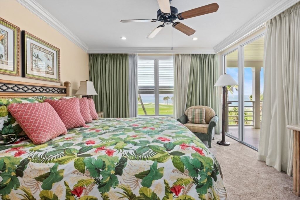 Un dormitorio con cama, ventilador de techo, una silla y vistas al exterior.