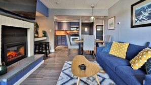 Una sala de estar moderna con chimenea, un sofá azul y un comedor al fondo.