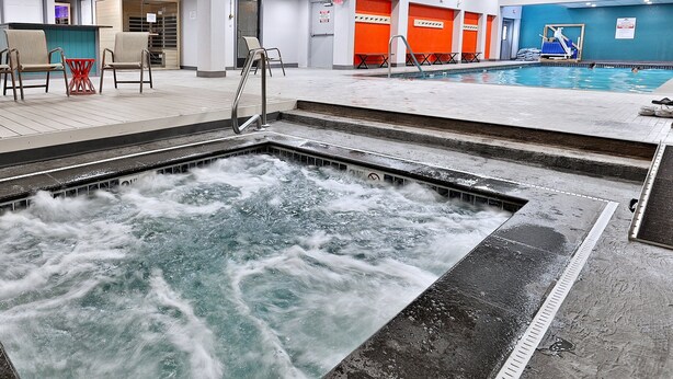 Piscina interior con zona de hidromasaje, asientos y vestuario con taquillas naranjas.